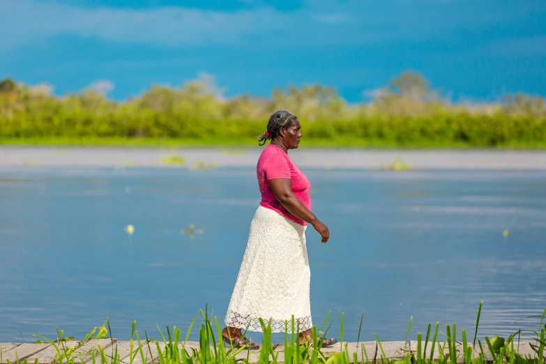 a woman in a skirt walking on sand by a river