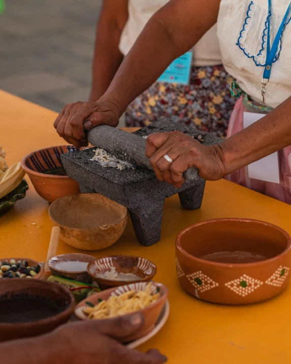 an older woman uses a stone to pour some brown liquid into her bowl