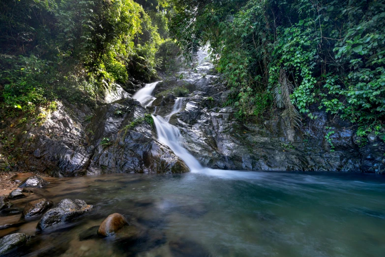 a waterfall near a lake in the middle of the forest