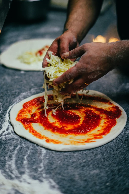 two people making pizzas in an outdoor kitchen