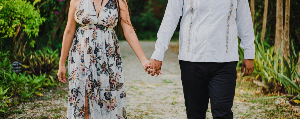 young couple holding hands walk along a path between a forest