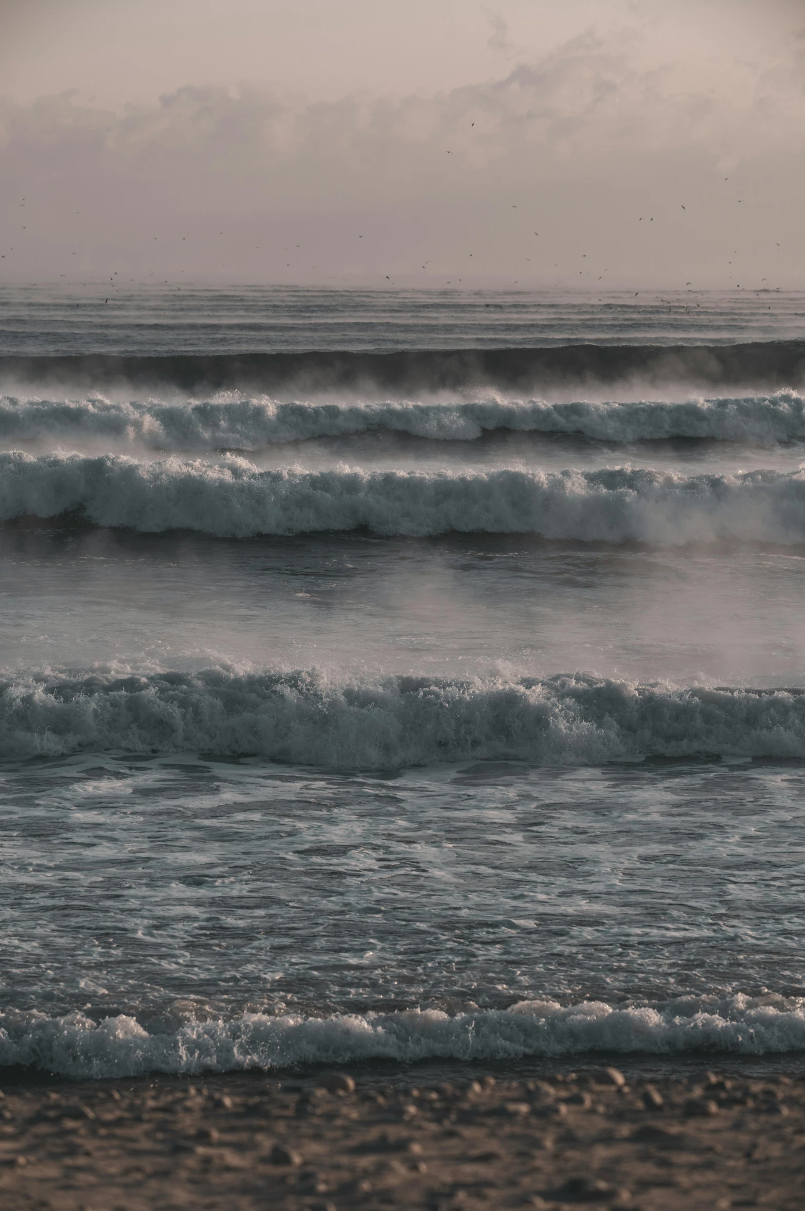 two men walking on a beach while the water is getting a little rough