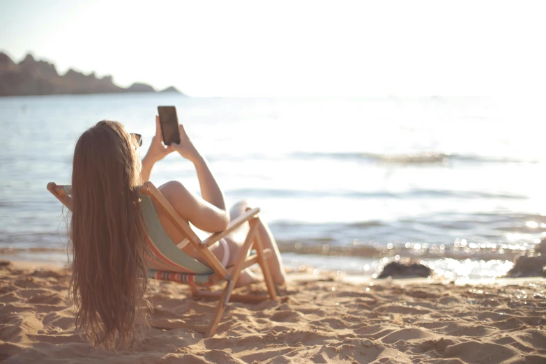 woman in a chair sitting on the beach using her cell phone