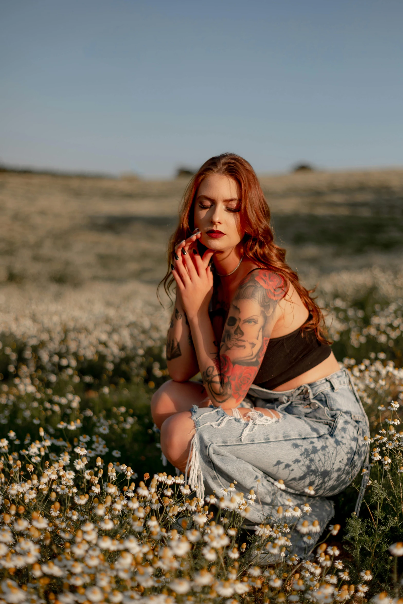 woman with tattoo kneeling in a field of flowers