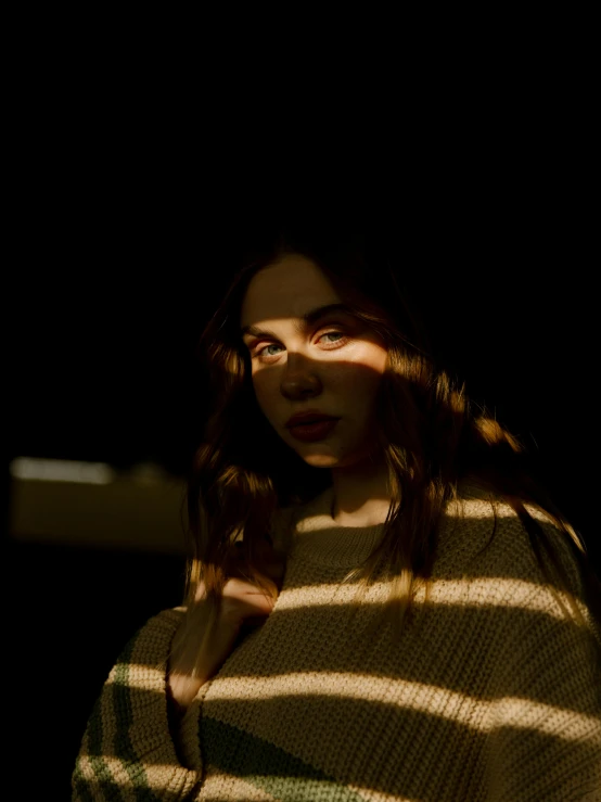 a woman wearing a sweater is standing in the shadows