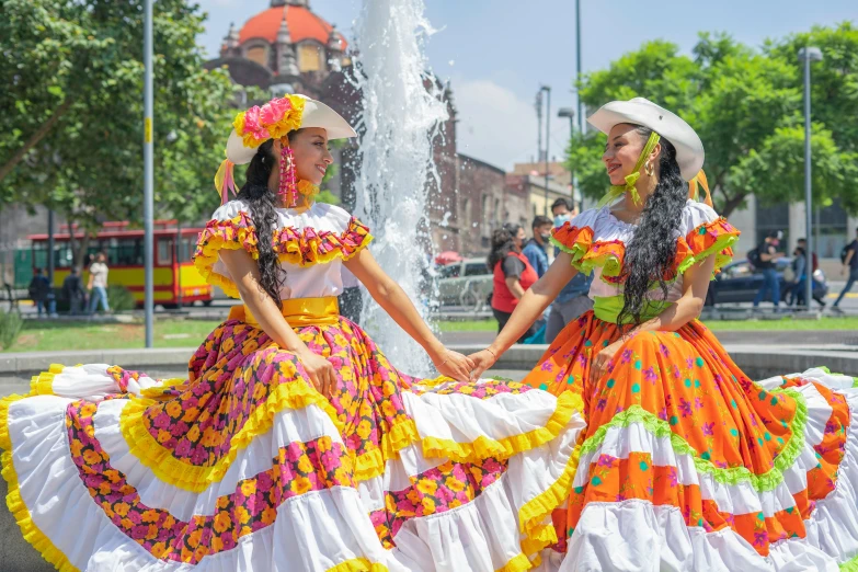 two women wearing colorful dresses and hats walking in the park