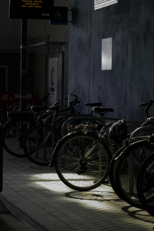 many bicycles are parked in the sun near a wall