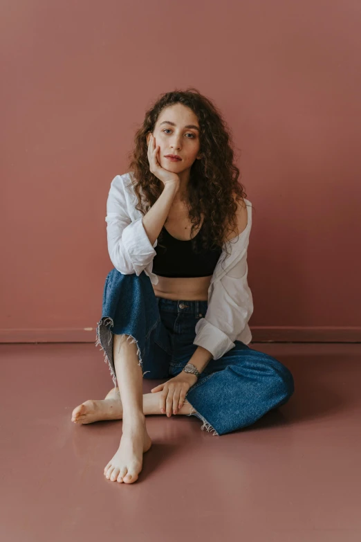 a young woman sitting on the floor in jeans and a cropped top