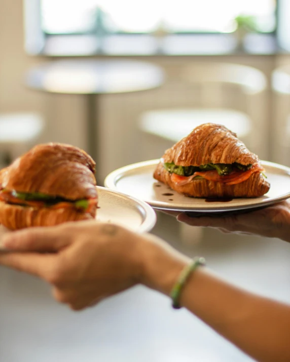 hands holding pastries on white plates with wooden table in background