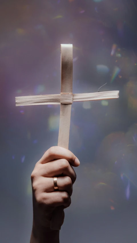 a hand holding a paper cross over a blue background