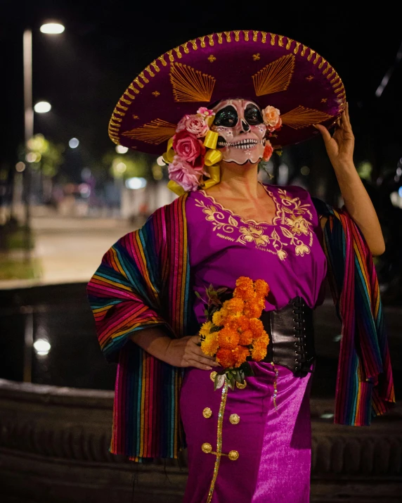 a woman in costume and a skull mask is holding an orange flower