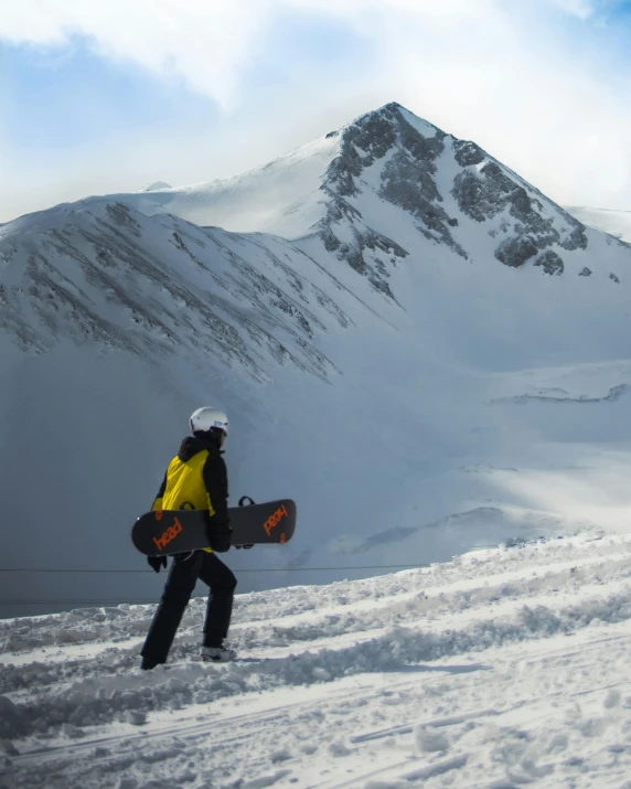 a man in black and yellow jacket holding a snowboard standing on snow covered field