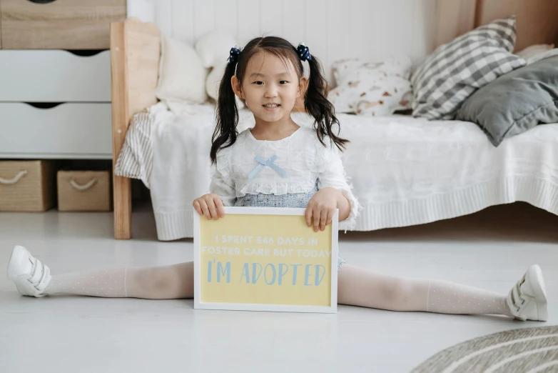 an adorable little girl sitting on the floor holding a sign
