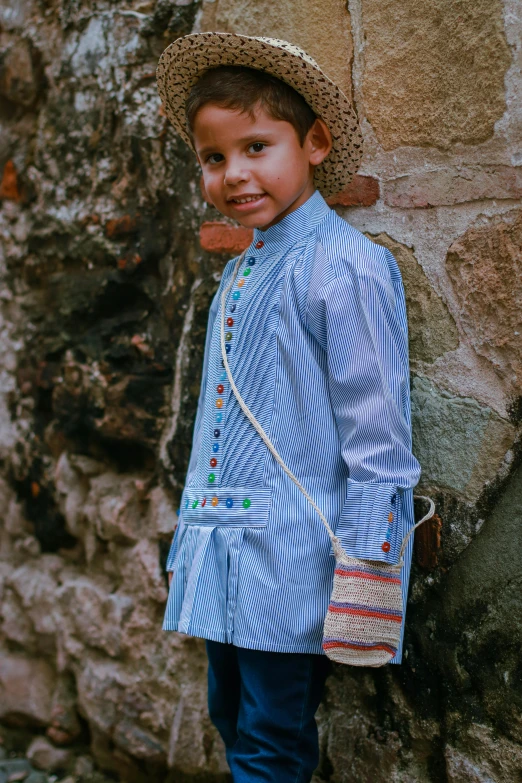 a  dressed in a blue striped outfit stands against a stone wall