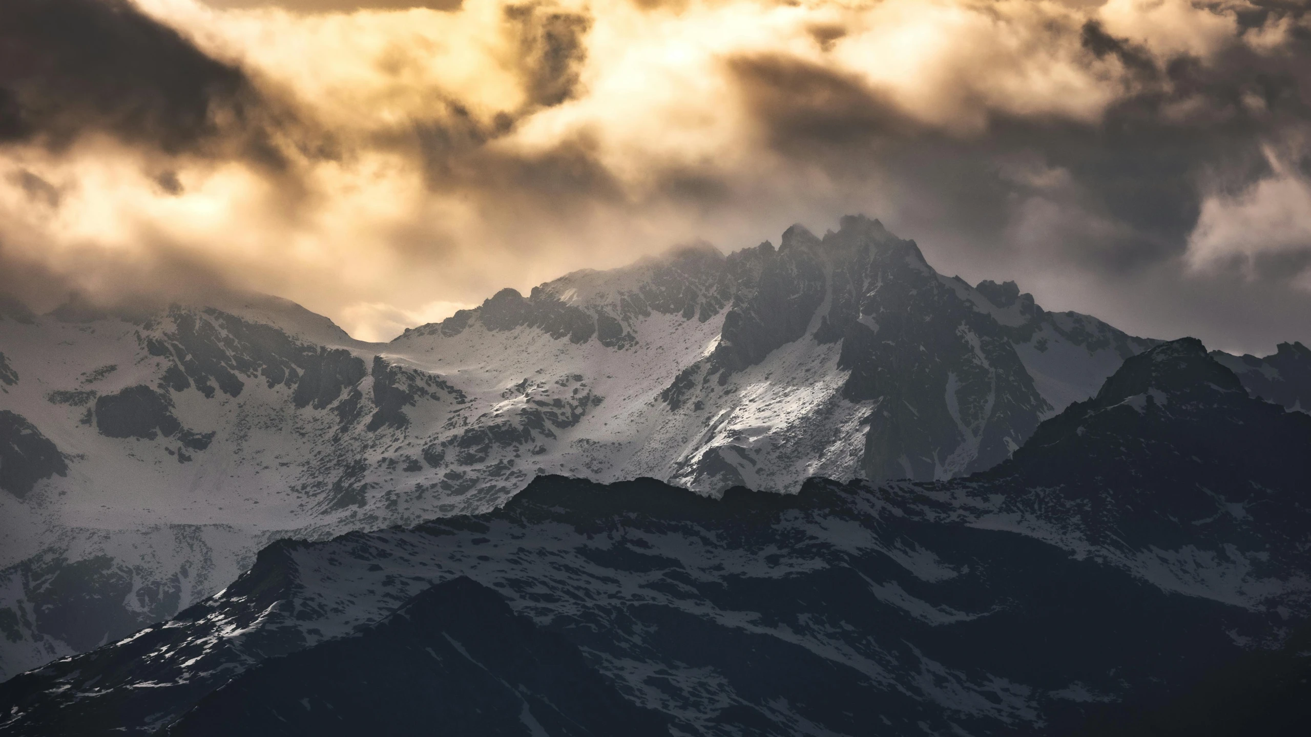 the snow covered mountains are in the foreground as clouds hover above them