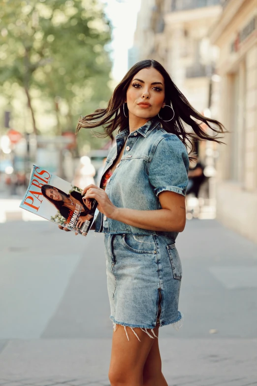 a young woman in a denim dress holding some shoes and looking into the camera