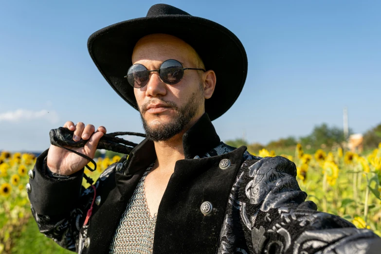 a man wearing a hat and glasses poses for a picture in the sun