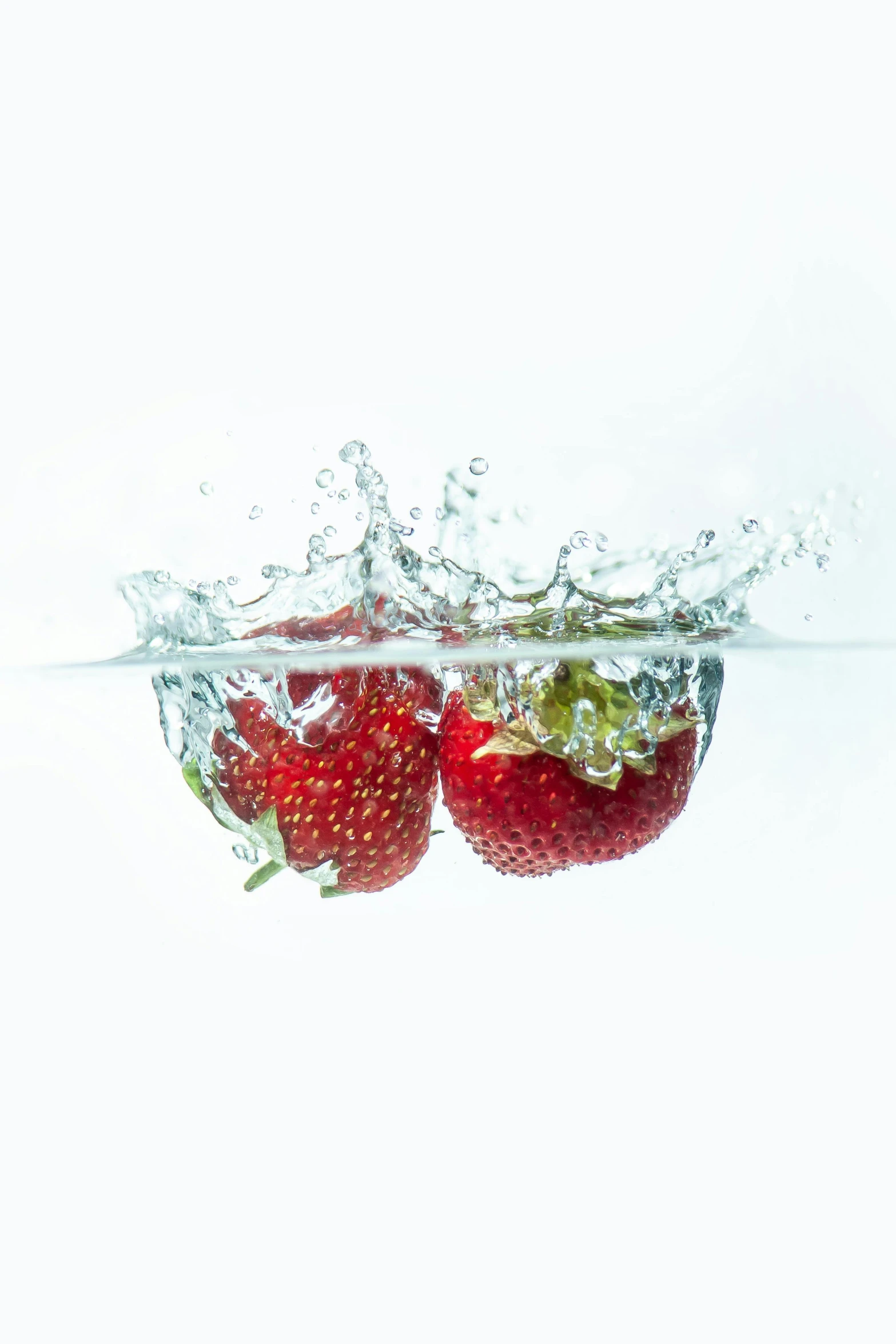 three strawberries with fruit splashing into the water