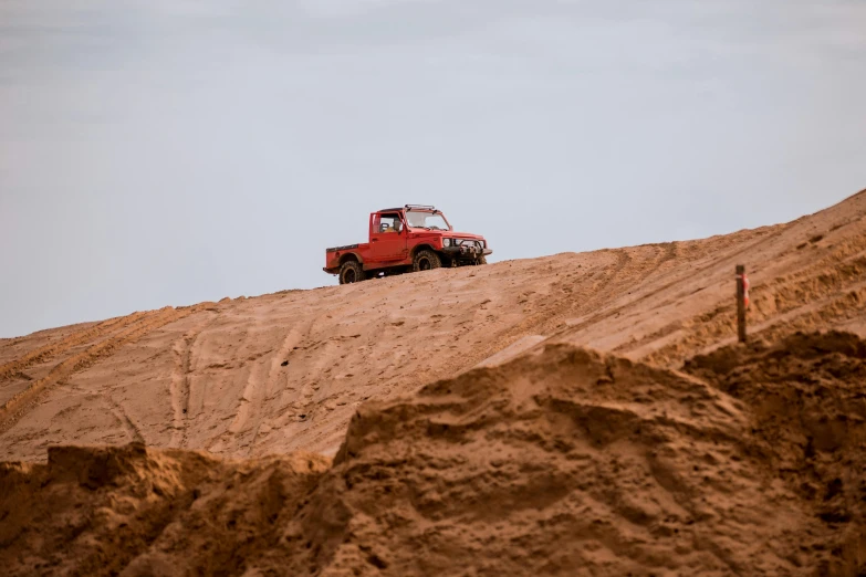 a red car sits on top of a sandy hill