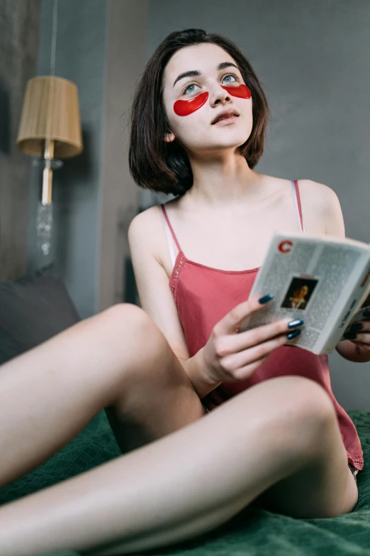 a woman with fake lipstick sits on her bed reading a book