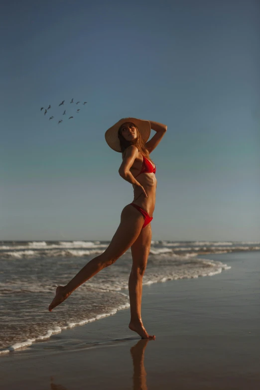 woman in red bikini and hat on beach with waves