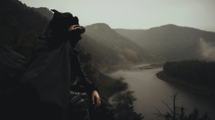 person standing on ledge holding soing in hand over looking water and mountain range