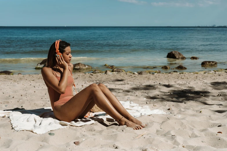 a woman is sitting on the sand talking on her phone