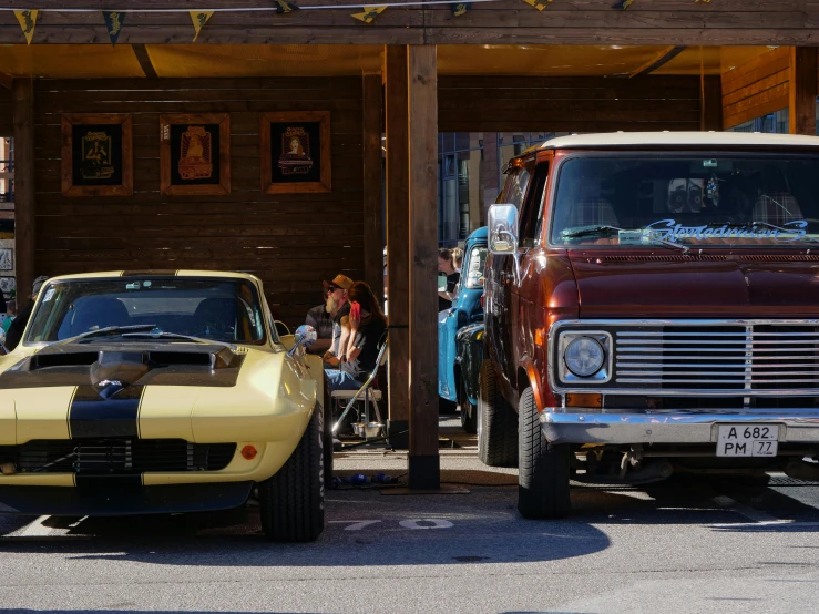 an old yellow car sits in the driveway with an older red car