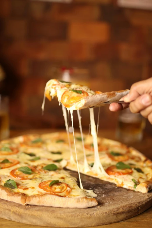 a hand holding up a piece of pizza from a wooden  board