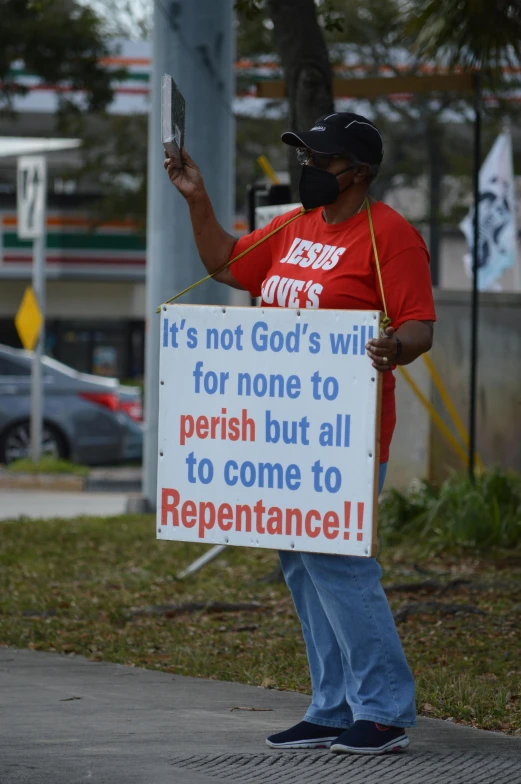 a person wearing a red shirt holds a sign that says it's not god's will for none to perish but all to come to repentance