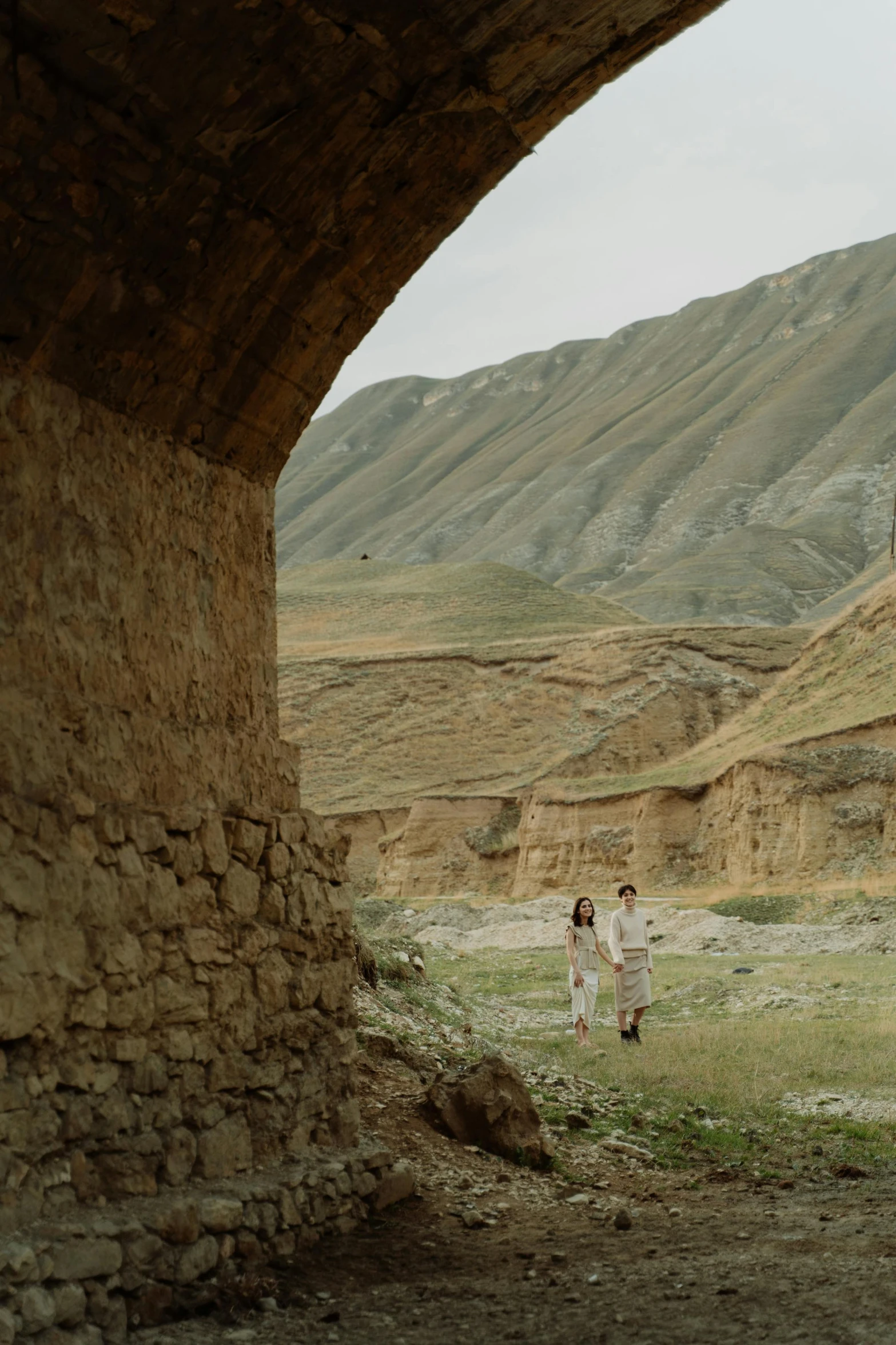 a young woman is walking under a bridge in a barren area