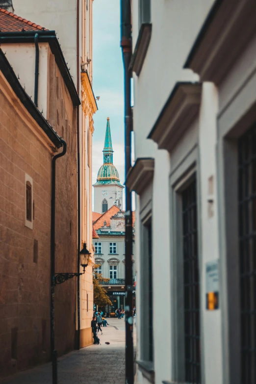 a narrow alley with houses and clock tower in the background