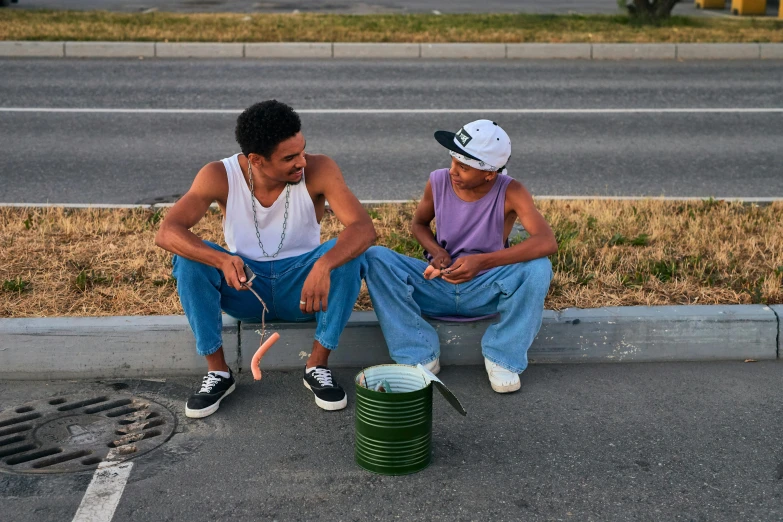 two young people sitting on the side walk, one with his hat and the other with his mouth open