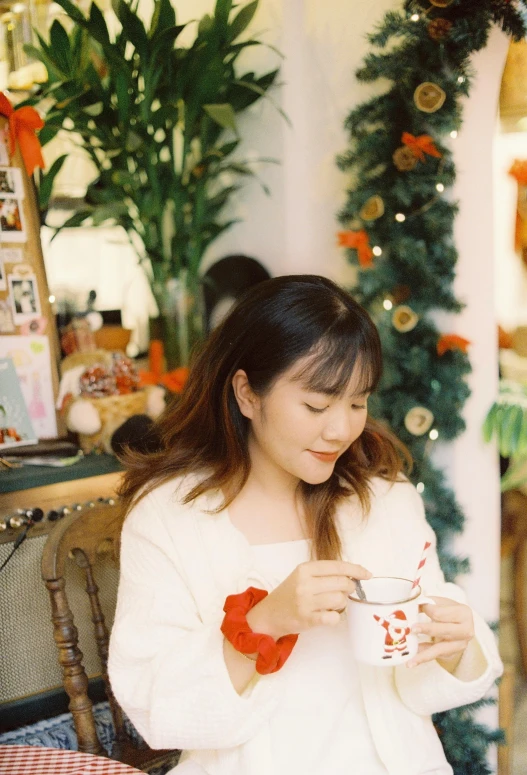 the young woman sits at a table holding a drink