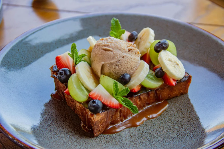 a piece of bread with a brown dessert, bananas, strawberries and chocolate sauce