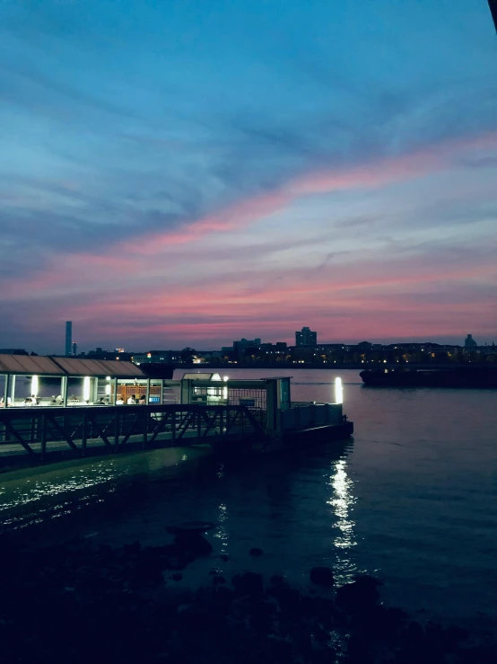 a dock is lit up at night while a beautiful pink sky is reflected in the water