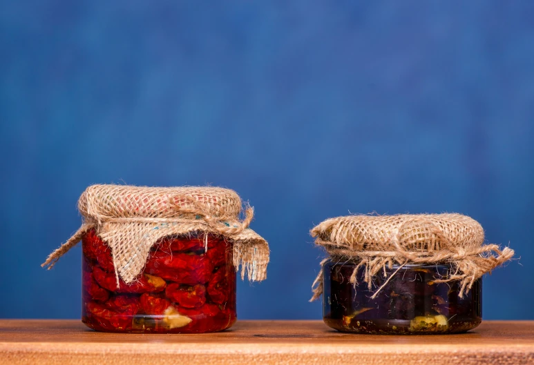 two jars filled with red and yellow fruit sitting on top of a wooden table