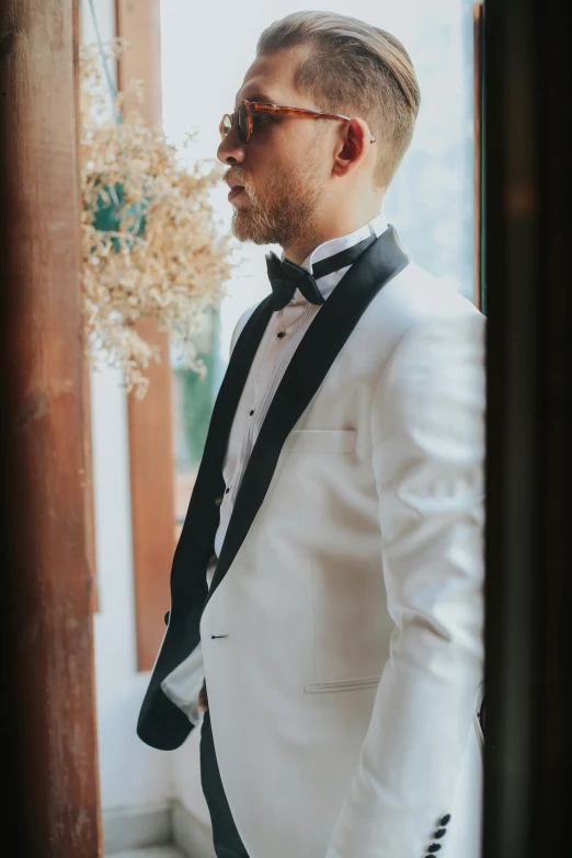 a man wearing a white tuxedo with glasses and a black bow tie