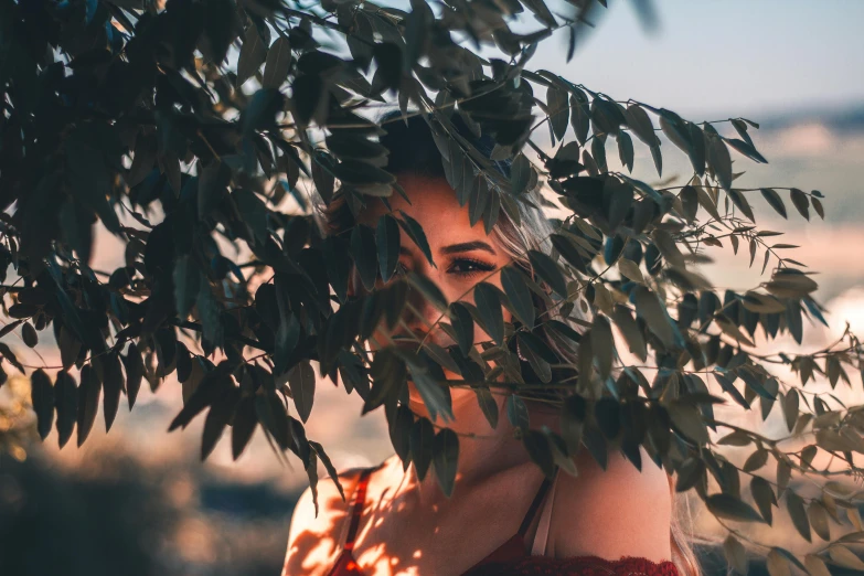 woman with red dress hiding her head behind a leafy tree