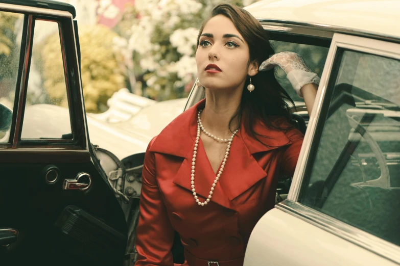 woman in red dress with long pearl necklace next to car