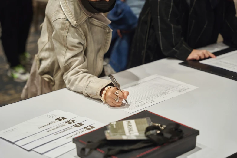 a man in a hoodie and face mask signing papers with a pen