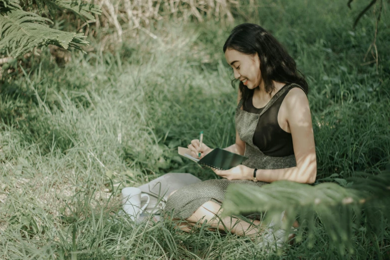 a young woman sitting on the ground writing