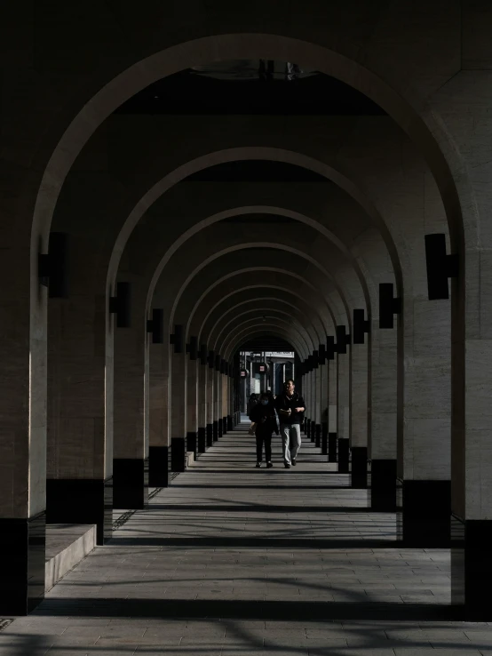 two people walk down an empty hallway under a bridge