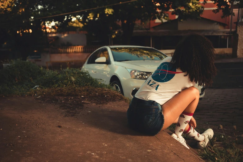 a woman sitting on a curb by her car at night