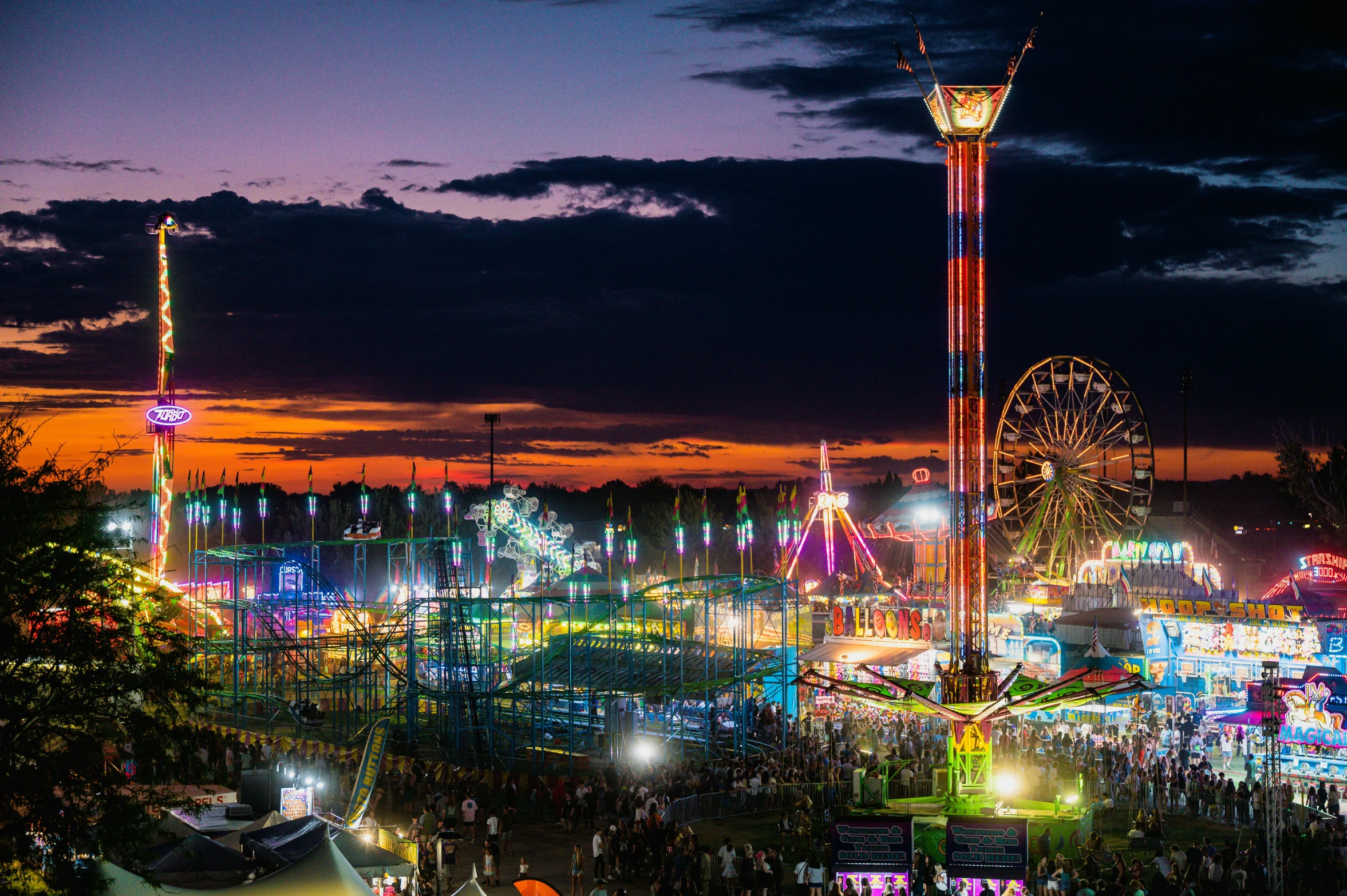 people gathered around a carnival with ferris wheel lights