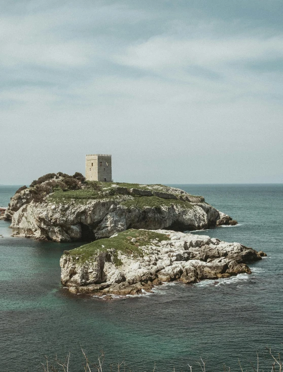 a stone tower with two small buildings on a rock island in the ocean