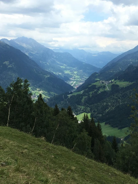 a lush green hillside surrounded by mountains under a cloudy sky