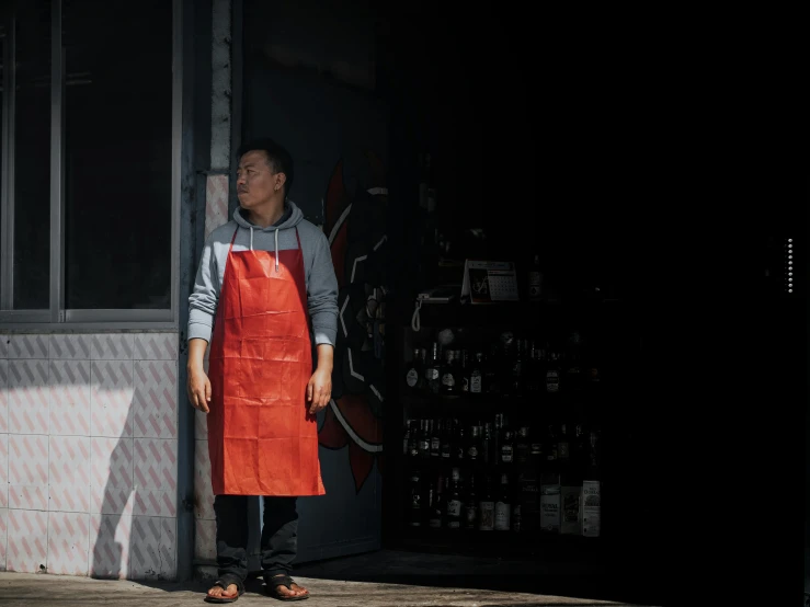 man with orange apron standing in front of store