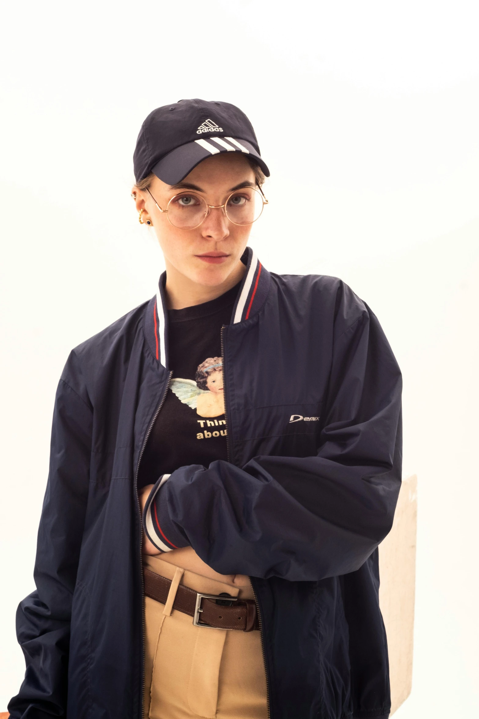 a woman wearing a hat and glasses standing in front of a white wall