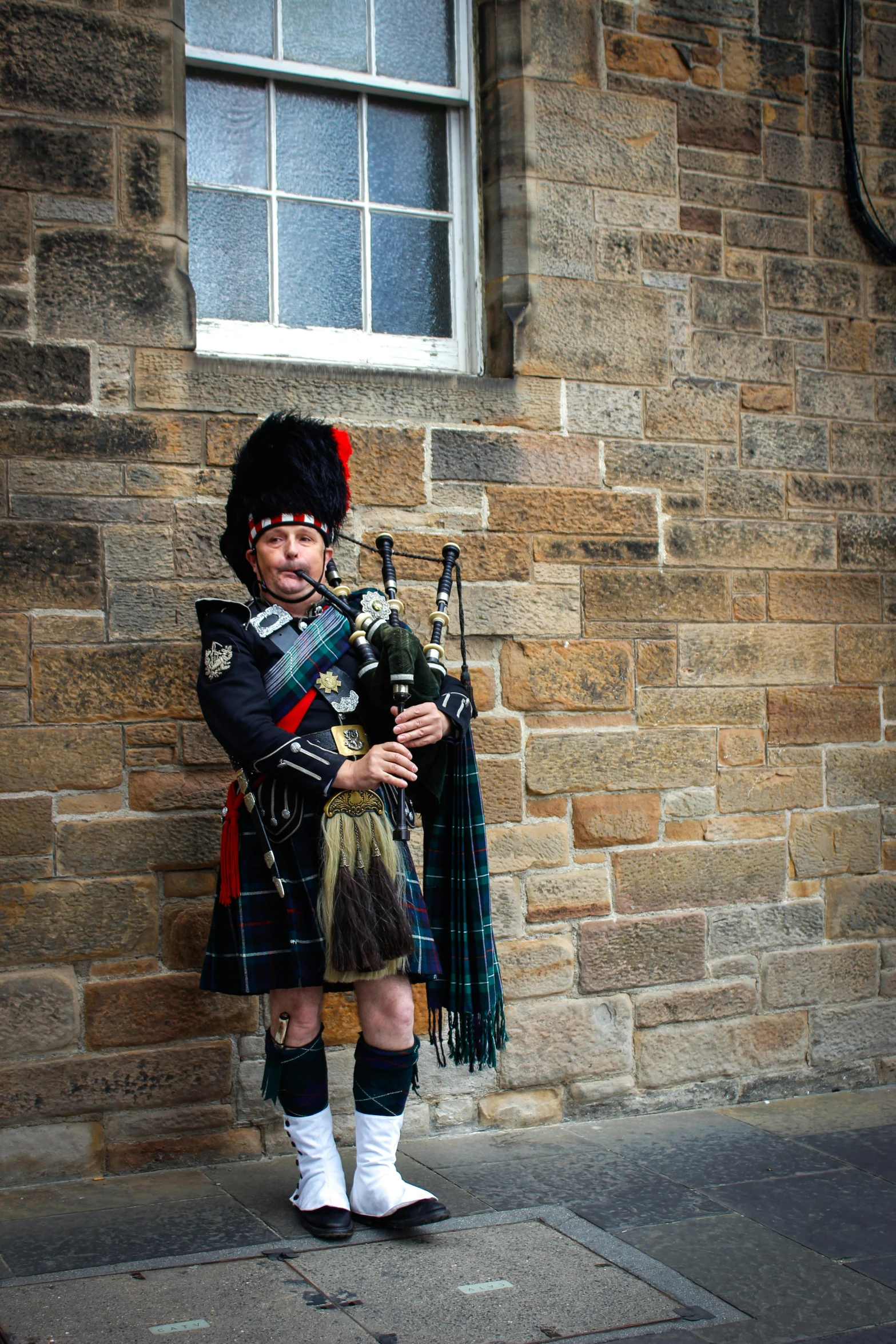 a man with a bagpipe in his hands, standing near a brick building